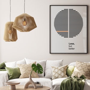 Op de afbeelding: Een witte bank met groene en beige kussens en een groene deken. Twee beige hanglampen hangen boven de bank. Een ingelijst print met een zwart-witte afbeelding en de tekst "Minder, maar beter" hangt aan de muur achter de bank.