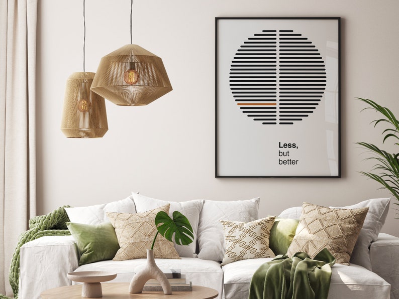 Op de afbeelding: Een witte bank met groene en beige kussens en een groene deken. Twee beige hanglampen hangen boven de bank. Een ingelijst print met een zwart-witte afbeelding en de tekst "Minder, maar beter" hangt aan de muur achter de bank.