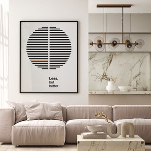 Op de afbeelding: Een woonkamer met een beige hoekbank, een salontafel met boeken en decoratieve voorwerpen en een zwart ingelijst print met een geometrisch ontwerp en de tekst "Minder, maar beter".