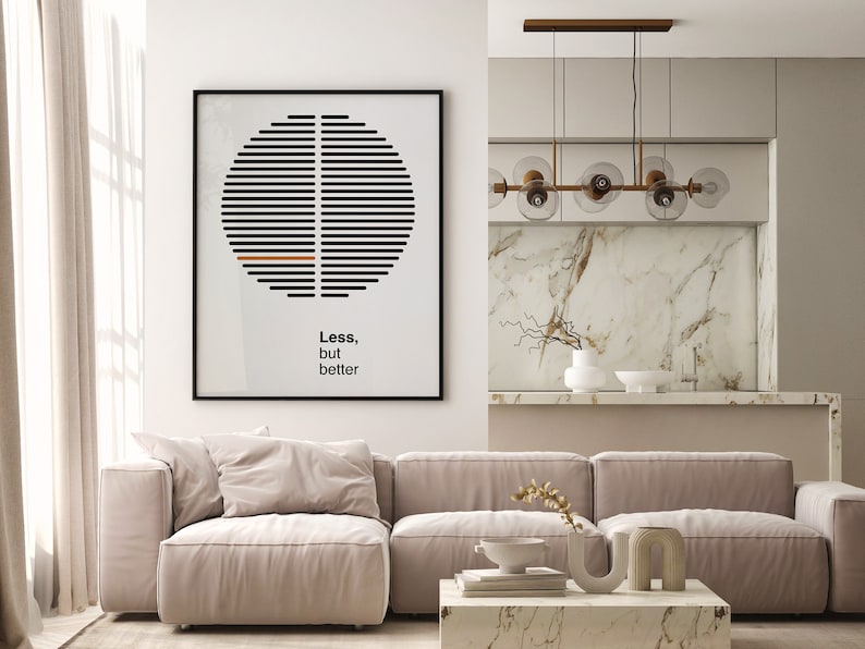 Op de afbeelding: Een woonkamer met een beige hoekbank, een salontafel met boeken en decoratieve voorwerpen en een zwart ingelijst print met een geometrisch ontwerp en de tekst "Minder, maar beter".