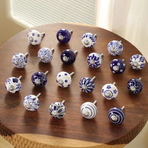 May include: A collection of decorative ceramic cabinet knobs in various designs. The knobs are primarily white and navy blue, featuring floral and geometric patterns. Each knob has a silver-toned metal stem.