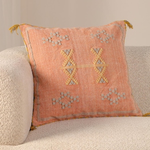 May include: A peach-colored throw pillow with a geometric pattern in yellow and gray. The pillow has a fringe trim.
