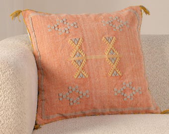 May include: A peach-colored throw pillow with a geometric pattern in yellow and gray. The pillow has a fringe trim.