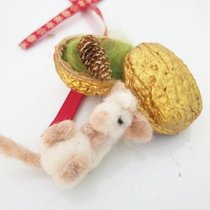 Könnte beinhalten: Ein weißes und braunes Filz-Maus-Ornament mit einer goldbemalten Walnussschale und einem kleinen Tannenzapfen im Inneren.