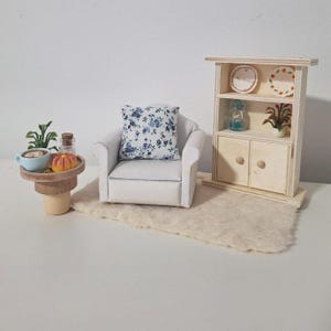 以下が含まれることがあります： ミニチュアのドールハウス家具セット。 花柄のクッションが付いた白いアームチェア、コーヒーカップとカボチャのある小さな木製サイドテーブル、棚付きの木製キャビネットが含まれています。 アームチェアの前には小さなラグがあります。