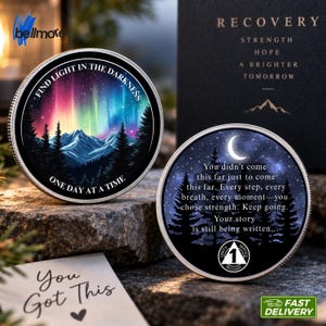 Può includere: Due monete circolari color argento. Una moneta presenta un'aurora boreale colorata sopra le montagne con il testo "FIND LIGHT IN THE DARKNESS" e "ONE DAY AT A TIME". L'altra moneta mostra una luna crescente, alberi e del testo.