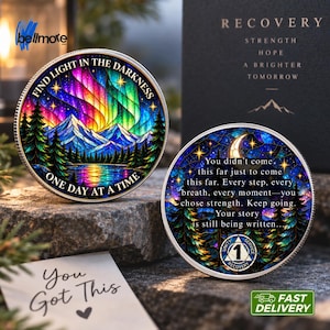 Può includere: Due monete circolari in metallo per il recupero con disegni colorati in stile vetrata. Una moneta raffigura un paesaggio montano sotto un'aurora boreale con il testo "Find light in the darkness, one day at a time". L'altra mostra una luna crescente e una foresta con il testo "You didn't come this far just to come this far. Every step, every breath, every moment—you chose strength. Keep going. Your story is still being written" e un simbolo "1".