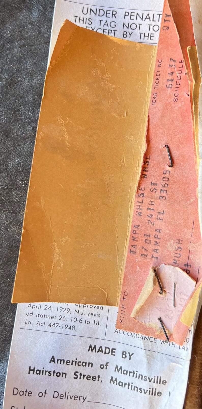 Puede incluir: Primer plano de ef&iacute;meras de papel vintage, que incluyen una etiqueta naranja rasgada y un boleto rosa. El texto incluye "TAMPA WHLSE WHSE" y "American of Martinsville". El papel est&aacute; envejecido y grapado.
