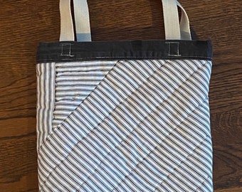 Op de afbeelding: Een zwart-wit gestreepte tote bag met een zwarte canvas bodem en witte canvas hengsels.