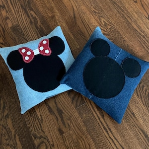 May include: Two denim pillow covers with black felt appliques of Mickey Mouse and Minnie Mouse. The Minnie Mouse pillow has a red bow with white polka dots.