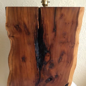 May include: A rustic wooden lamp base with a natural wood finish and a large crack running down the center. The base is made from a single piece of wood with a live edge.