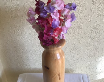 May include: A wooden vase with a natural finish, featuring a wide mouth and a slender body. The vase is filled with a bouquet of pink, purple, and red sweet pea flowers.