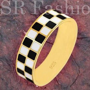 May include: Gold-colored ring with a checkerboard pattern of black and white squares. The ring is marked with "925" and the text "SR Fashion" is visible in the background.