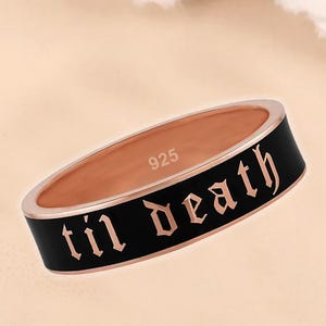 May include: A rose gold ring with a black band featuring the phrase "til death" in a gothic font. The ring is marked with "925" inside the band. The ring is a piece of jewelry.