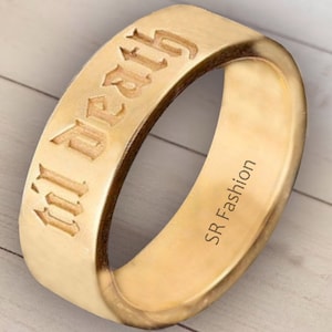 May include: A gold-colored ring with the words "'til death" engraved in a gothic font. The inside of the ring is engraved with "SR Fashion".