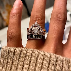 以下が含まれることがあります： ダイヤモンドリングのコレクション。王冠型のリングと「til death」と刻まれたバンドが含まれています。指に装着され、複雑なディテールと輝く石が際立っています。リングは金と銀の色です。