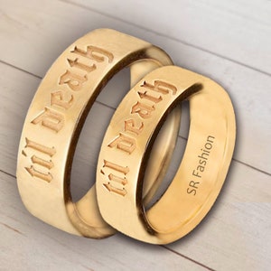 May include: Two gold-colored rings with the words "till death" engraved in a gothic font. The rings are stacked on top of each other.