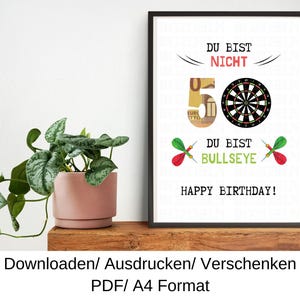 Może przedstawiać: Drukowana kartka urodzinowa z tarczą do rzutków i tekstem "Du bist nicht 50, Du bist Bullseye! Happy Birthday!" w języku niemieckim.