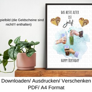 May include: A framed print with the text "DAS BESTE ALTER IST jetzt HAPPY BIRTHAY" and illustrations of drinks and hands. The print has a black frame and is displayed on a wooden shelf. A potted plant is in the foreground.