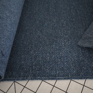 May include: Close-up of a dark blue fabric with a textured surface. The fabric is rolled up on the left side and folded over on the right side. The fabric is sewn together with a white thread.