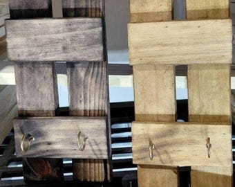 May include: Two wooden key holders, one stained dark brown and the other light brown. Each has two brass-colored hooks. The key holders are made of rectangular wooden slats and are mounted on a metal rack.