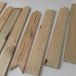 May include: A collection of unfinished wooden planks, varying in length and width, with natural wood grain patterns. Some planks have pointed or angled tops, while others are rectangular. The wood has a light, natural color.