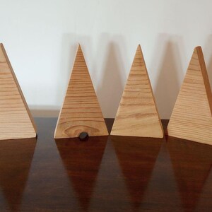 May include: Seven wooden triangle-shaped ornaments in various sizes, arranged in a row on a dark brown surface. The ornaments are made of light brown wood and have a natural finish.