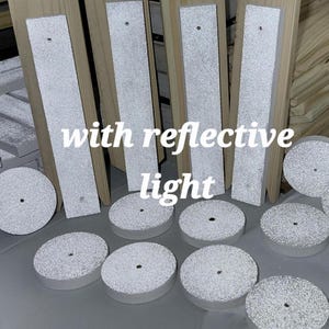 May include: A collection of unfinished light-colored wooden rectangular planks and circular discs with white textured surfaces that feature reflective light properties. Each piece contains a small centered hole. The text with reflective light is visible.