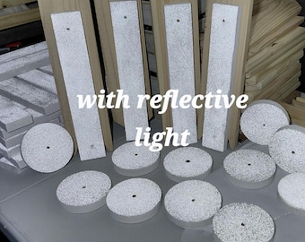 May include: A collection of unfinished light-colored wooden rectangular planks and circular discs with white textured surfaces that feature reflective light properties. Each piece contains a small centered hole. The text with reflective light is visible.