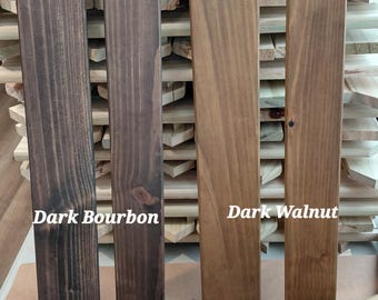 May include: Four wooden fence pickets in varying shades of brown, labeled "Dark Bourbon" and "Dark Walnut." The pickets are displayed against a backdrop of unfinished wood slats, showcasing the different stain colors.