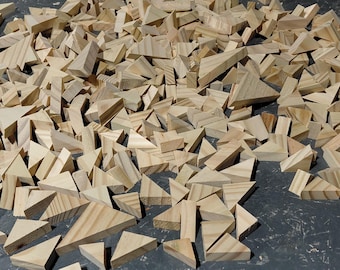 May include: A collection of small, unfinished wooden triangles scattered on a dark surface. The triangles vary in size and shape, with visible wood grain. The natural wood color creates a warm, earthy tone, suggesting a craft or building project.