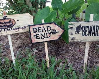 May include: Three wooden Halloween signs with text and graphics. One sign says "HAPPY HALLOWEEN" with a jack-o'-lantern and spiders. Another says "DEAD END" with a skull. The third says "BEWARE" with rat silhouettes.