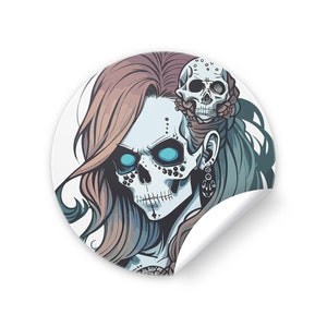 May include: A round sticker with a colorful illustration of a woman with a skull face and a small skull with flowers in her hair.