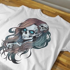 May include: White t-shirt with a colorful graphic print of a skull with blue eyes and a floral design. The skull is surrounded by long, flowing hair.
