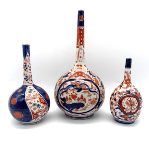 May include: Three ceramic vases with long, slender necks and rounded bodies, decorated with intricate patterns in shades of deep blue and vibrant orange-red against a white background, featuring floral motifs and geometric shapes.