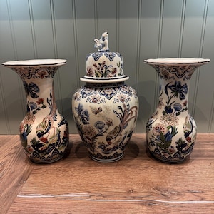 Può includere: Tre vasi decorativi in ceramica con motivi floreali blu e bianchi. Il vaso centrale ha un coperchio con un pomo a forma di uccello.