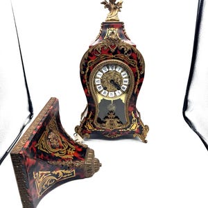 May include: An antique clock with a tortoiseshell finish and ornate gold accents. The clock face is white with black Roman numerals and gold hands. A matching wall shelf is also present.