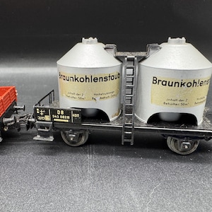 Könnte beinhalten: Ein Modell-Eisenbahnwagen mit zwei silbernen zylindrischen Behältern mit der Aufschrift "Braunkohlenstaub" und einem roten Güterwagen. Der Wagen hat ein schwarzes Fahrgestell mit Rädern und eine Leiter zwischen den Behältern.
