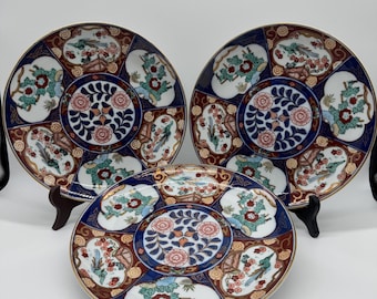 Può includere: Tre piatti decorativi in ceramica con un motivo floreale e di uccelli. I piatti presentano un bordo blu con accenti rossi, bianchi e verdi. I piatti sono esposti su supporti neri.