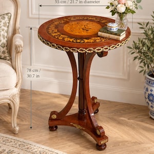 May include: A round wooden pedestal table with a diameter of 21.7 inches and a height of 30.7 inches. The tabletop features intricate floral marquetry inlay and a gold-toned metal trim. The base consists of three curved legs with gold accents.