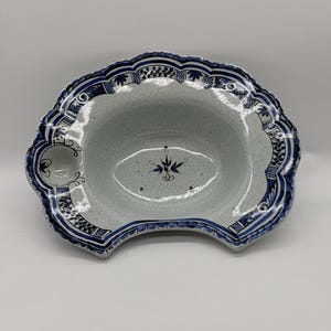 Op de afbeelding: Ovale keramische serveerschaal met een geschulpte rand. De schaal heeft een wit interieur met een craquelé glazuur en is omrand met een blauw-wit bloemmotief. De schaal heeft aan één kant een klein handvat.