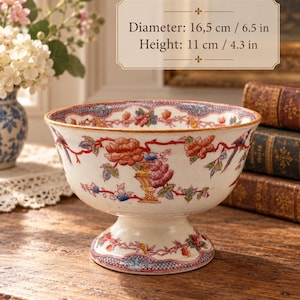 Pode incluir: Uma taça de cerâmica cor de creme com base, apresentando um padrão colorido de flores e pássaros em vermelho, laranja, azul e verde. A taça tem 16,5 cm de diâmetro e 11 cm de altura, com uma borda decorativa ao longo do rebordo e da base.