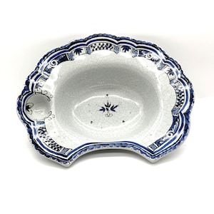 Op de afbeelding: Een geschulpte keramische kom met een witte craquelé glazuurafwerking, voorzien van gedetailleerde blauwe handgeschilderde bloem- en geometrische patronen langs de rand en een centraal blauw bloemmotief. De kom heeft een kleine ronde inkeping.