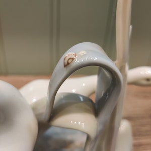May include: A ceramic sculpture of a swan with a blue and white glaze. The swan's neck is curved and the head is tilted to the side. The swan is standing on a base with a brown and white glaze.