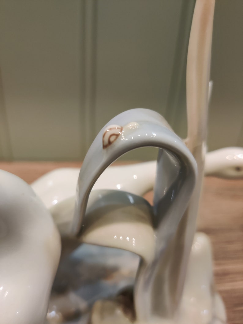 May include: A ceramic sculpture of a swan with a blue and white glaze. The swan's neck is curved and the head is tilted to the side. The swan is standing on a base with a brown and white glaze.
