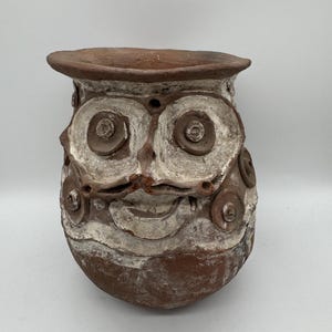 Könnte beinhalten: Handgefertigter, terrakottafarbener Topf in Eulenform mit einem breiten, lächelnden Gesicht. Der Topf hat große, kreisförmige Augen und dekorative Akzente in weißer Farbe. Der Topf hat einen abgerundeten Körper und einen ausgestellten Rand, ideal für Pflanzen.