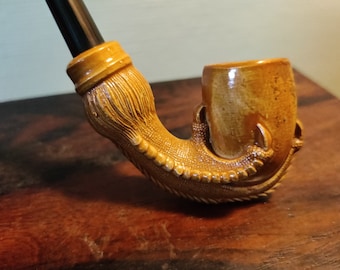 May include: A brown ceramic pipe shaped like a dragon's claw. The pipe has a black stem and a bowl that is slightly wider than the stem.