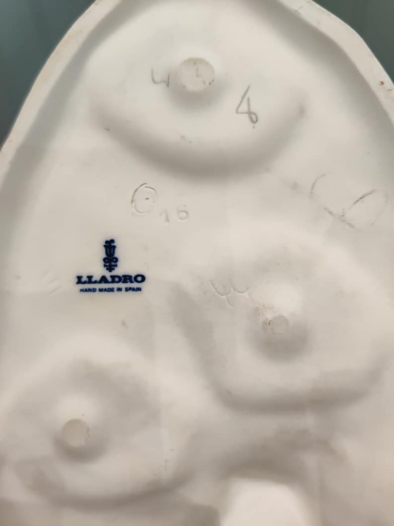 May include: The bottom of a white porcelain figurine with a blue and white Lladro logo that reads "Lladro Hand Made in Spain". The figurine is marked with the number "416" and the number "4" is written in pencil.