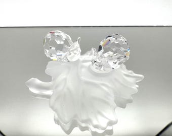 May include: Two crystal snail figurines with faceted bodies sit atop a frosted glass leaf. The snails' bodies reflect light, creating a sparkling effect. The leaf has a delicate, textured appearance, adding to the overall elegance of the decorative piece.