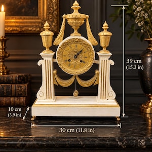 May include: A mantel clock with a gold-toned face, Roman numerals, and black hands. The frame is white with gold accents, featuring two columns and decorative finials. It measures 39 cm high, 30 cm wide, and 10 cm deep.